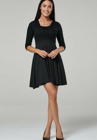 Black dress with a fitted bodice, three-quarter sleeves, and a flared skirt featuring a white polka dot pattern. Smooth fabric texture, minimalist design.