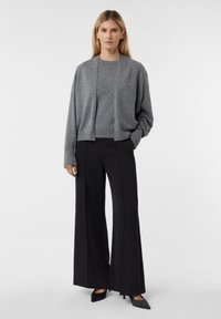 Szary kardigan z wełny na szarym swetrze, zestawiony z czarnymi spodniami o szerokich nogawkach. Tkanina jest miękka, z minimalnie widocznymi szwami i luźnym krojem.