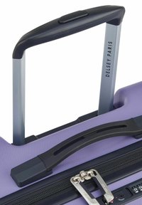 Valigia rigida viola con superficie testurizzata, dotata di manico telescopico, accenti neri e una combinazione di lucchetto attaccato alla cerniera.