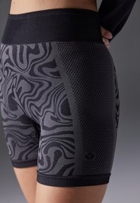 Musta urheilushortsit, joissa on teksturoitu aaltokuvio. Sisältävät verkkokankaatyylisen yksityiskohdan ja paksun, tukevan vyötärökaitaleen.