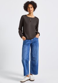 Donker, gladde blouse met lange mouwen en een keyhole-halslijn; gecombineerd met wijde blauwe denim jeans en witte sneakers.