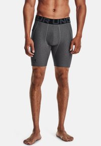 Shorts de sport ajustés gris avec une ceinture élastique noire, arborant un logo et une texture lisse. Design mi-cuisse.