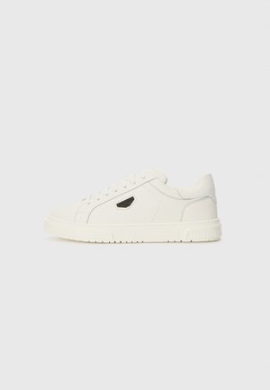 Sneaker bianco in pelle con finitura liscia, lacci piatti e un accento logo nero. Caratterizzato da una suola in gomma testurizzata e design del toe arrotondato.