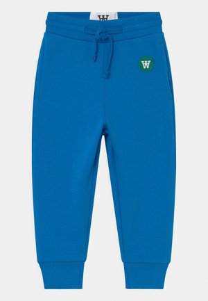 Calças de fato de treino azuis feitas de um suave misto de algodão, com um cós elástico, cordão, bolsos laterais e um emblema verde.