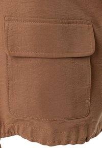 Brauner Stoff mit glatter Textur, der mit einer rechteckigen Tasche versehen ist. Nahtdetails und ein geraffter Saum am unteren Ende ergänzen das Design.