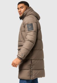 Nahrbtnik rjav parkas plašč s kapuco, ki ima značko z logotipom na rokavu, pritisne gumbe na straneh in rebraste manšete.