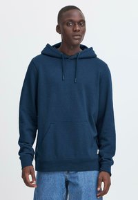 Felpa blu navy realizzata in tessuto misto cotone, caratterizzata da una tasca frontale, cappuccio con cordino, polsini a costine e una superficie leggermente struttura.