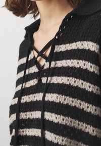 Schwarz-beige gestreifter Stricktop mit einer Schnürneckline, strukturiertem Garn und einem kragenförmigen Design, das offene Maschen-Details aufweist.