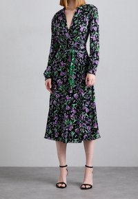 Černé šaty s dlouhými rukávy, zdobené fialovým a zeleným květinovým vzorem, a s páskem v oblasti pasu. Nosené s černými sandály na podpatku.