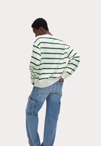 Vit sweatshirt med gröna horisontella ränder, avslappnad passform och ribbade ärmslut. Ljust blå cargobyxor med flera fickor, bärs vid midjan.