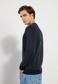 Suéter de punto de color navy con patrón texturizado, puños y dobladillo acanalados, cuello redondo, diseño ajustado, combinado con jeans de color azul claro.
