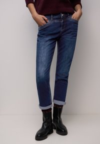 Donkerblauwe denim jeans met een mid-rise en een rechte pasvorm, voorzien van opgerolde pijpen. Voorzien van zijzakken en contrasterende stiksel details.