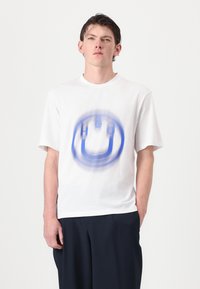 T-shirt blanc à manches courtes avec un motif graphique circulaire bleu au centre. Fabriqué en coton, il a un col rond et une coupe décontractée.