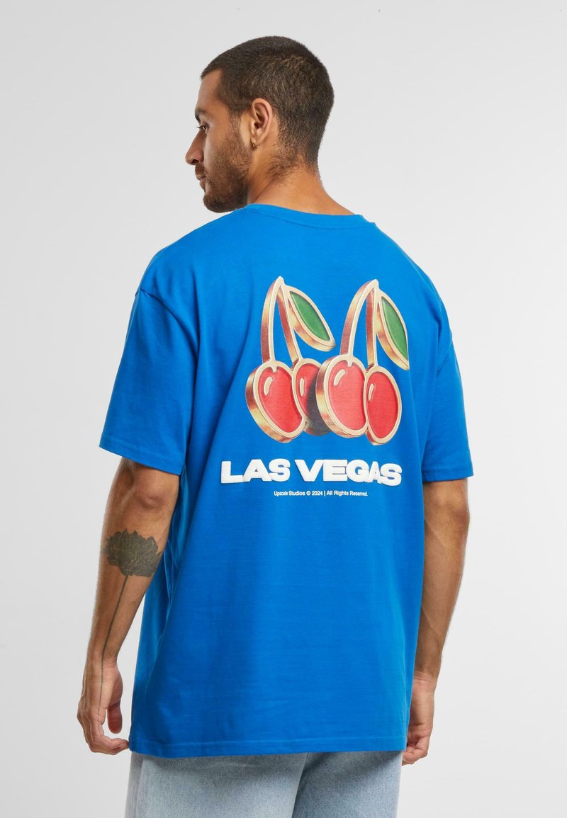 Mėlyna medvilninė marškinėliai su didelėmis vyšnių grafikomis ir užrašu "LAS VEGAS" ant nugaros. Trumpomis rankovėmis ir laisvu siluetu.