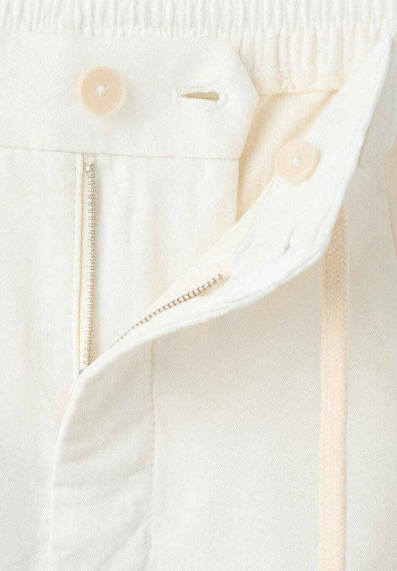 Pantalon écru avec une fermeture éclair ouverte, deux boutons visibles et une ceinture partiellement repliée.
