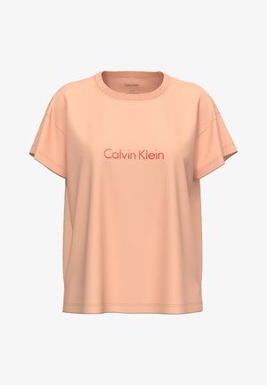 Brzoskwiniowy t-shirt z krótkim rękawem, z okrągłym dekoltem i czerwonym wyszywanym logo „Calvin Klein” na środku z przodu.