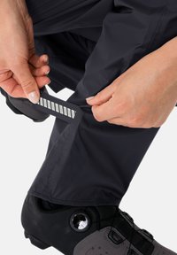 Pantalons noirs résistants aux intempéries avec un accent réfléchissant sur l'ourlet, ajustés pour s'adapter à de solides chaussures de sport. Texture lisse et design léger.