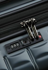 Zwarte harde koffer met een gestructureerd oppervlak, dubbele ritsen en een TSA-goedgekeurd slot met een combinatie-draaiknop.