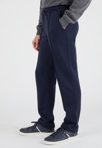 Pantalones de chándal azul marino hechos de una tela suave; cuentan con una cinturilla elástica con cordón, bolsillos laterales y un sutil detalle de costura.