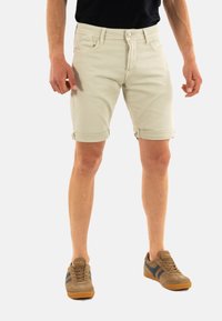 Lichtbeige denim shorts met opgerolde boorden, met een klassiek vijf-pocket ontwerp en een metalen knoopsluiting. Gemaakt in combinatie met bruine en marineblauwe sneakers.