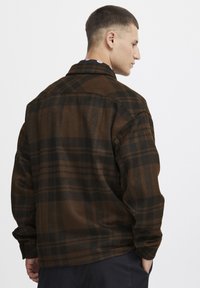 Chemise à carreaux brune et noire, fabriquée en tissu doux, dotée de manches longues, de poignets boutonnés et d'un design de dos ample.