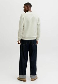 Lichtgrijze sweatshirt met geribde boorden, gecombineerd met donkere denim trousers die aan de onderkant zijn opgerold. De outfit heeft eenvoudige, strakke lijnen.