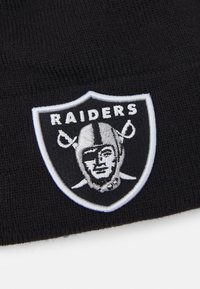 Gorro de punto negro que presenta un escudo bordado en blanco con un logo de Raider en plata y negro, y el texto "RAIDERS" encima.
