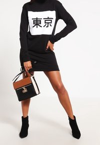 Musta pitkähihaisen mekko, jossa on valkoinen graafinen kuvasto, jossa on japanilaisia merkkejä; yhdistettyvärilohkottu käsilaukku mustana, tanina ja beigeinä.