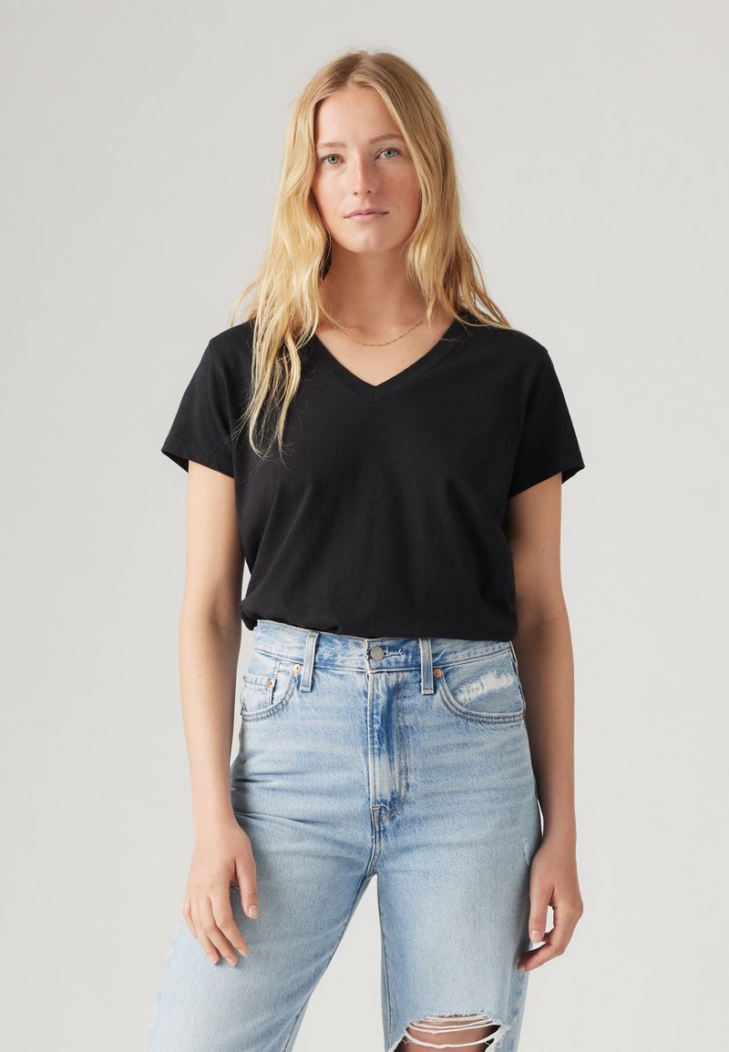 Tricou negru cu decolteu în V, fabricat din bumbac moale, cu mâneci scurte. Asortat cu blugi decolorați, cu talie înaltă, de culoare bleu deschis.