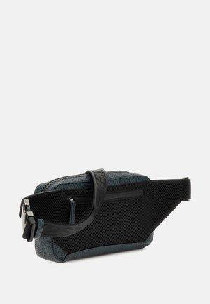 Banane en tissu texturé vert avec un dos en mesh, sangle noire avec un texte en relief et un compartiment à zip sur le dessus.