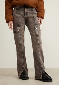 Jeans cargo sbiaditi con due tasche laterali, chiusura frontale con bottone e cuciture a contrasto. Indossati con stivali neri con piattaforma.