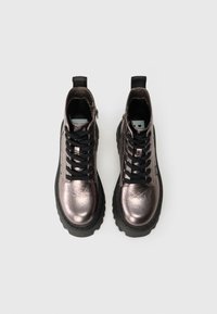 Un par de botas de cuero metálico plateado con cordones negros, suelas gruesas negras y cremalleras laterales sobre un fondo gris claro.