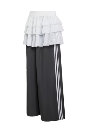 Athletic pants in dark gray with three white stripes on the sides, topped by a layered ruffled white overlay. Soft fabric, wide fit.