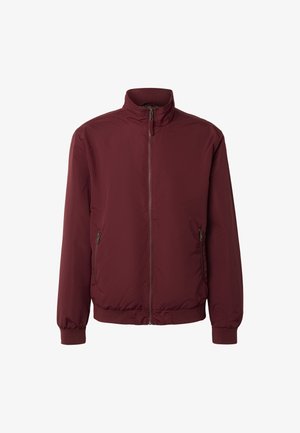 Bordó cipzáras kabát álló gallérral, rugalmas mandzsettákkal és két cipzáras oldalzsebbel, fehér háttéren bemutatva.