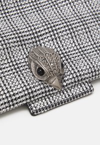 Černobílá texturovaná kabelka do ruky se stříbrným zapínáním ve tvaru ptáka s černými kamennými akcenty a vzorovaným látkovým povrchem.