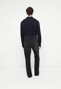 Tengerészeti hosszú ujjú póló szürke vállbetétekkel, sötét farmernadrággal párosítva. Fehér sportcipővel egészül ki az öltözet.