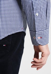 Camisa de manga larga con estampado de cuadros vichy azul y blanco, puños abotonados; presenta detalles en rojo en los puños y en el dobladillo lateral; tela de algodón.