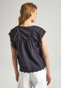 Blusa grigio scuro con maniche corte a volant con dettagli tagliati al laser, pannello posteriore arricciato e orlo scallop. Morbido tessuto di cotone.