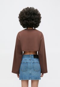 Braunes, kurz geschnittenes Langarmoberteil mit weitem Ausschnitt, kombiniert mit einem hellblauen Denim-Minirock mit Gesäßtaschen und einem schwarzen Logostreifen.