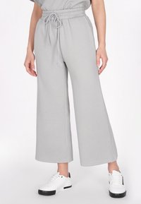Grijze wijde broek met een gestructureerd ruitpatroon, voorzien van een elastische tailleband en trekkoord. Gepaard met witte sneakers.
