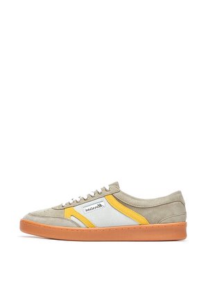 Zapatilla baja de ante beige con panel lateral blanco y amarillo, cordones blancos y suela de goma naranja, vista desde el lado exterior.