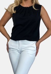 Musta hihaton toppi, jossa on pleatattu muotoilu, sileä rakenne ja väljä istuvuus, yhdistetty valkoisiin räätälöityihin housuihin, joissa on keskikorkea vyötärö.