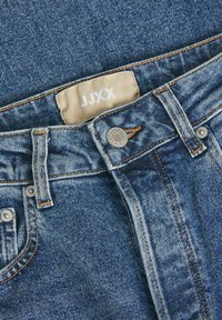 Jeans in denim di blu medio con cuciture arancioni, dotati di un bottone in metallo, chiusura con zip e un'etichetta del marchio cucita all'interno della vita.