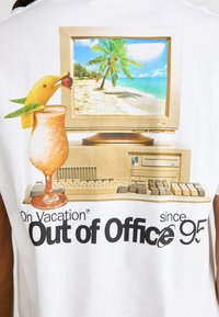 Weißes T-Shirt mit einem Grafikdesign, das einen Vintage-Computer, ein tropisches Getränk und eine Strandlandschaft zeigt, mit dem Text "Im Urlaub, außer Haus seit 95."