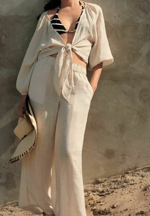 Haut court en lin à nouer sur le devant, associé à un pantalon large avec taille élastique. Couleur beige clair, texture lisse et design minimaliste.