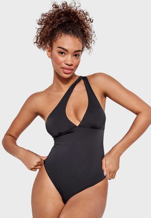 Bañador negro de una pieza con una sola tirante, escote en V profundo y piernas de corte alto. Tela suave con un detalle mínimo.