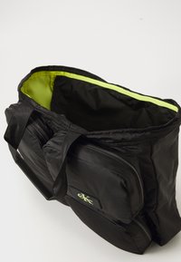 Black fabric bag with a vibrant lime green interior. Features multiple zippered compartments and fabric handles for carrying.