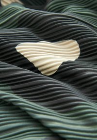 Tissu texturé avec un motif côtelé en vert foncé, noir et beige, présentant un grand cœur beige au centre.