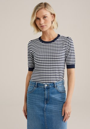 Niebiesko-biały pasiasty t-shirt z krótkim rękawem i okrągłym dekoltem, zestawiony z dżinsową spódnicą z rozcięciem z przodu i pięcioma kieszeniami.