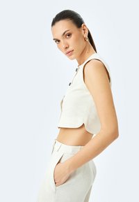 Beige Cropped-Leinenoberteil mit kurzen Ärmeln und schwarzen Knöpfen, kombiniert mit passenden hoch taillierten Hosen mit Seitentaschen.